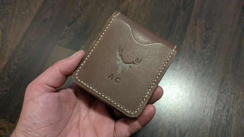 Compact brown leather wallet with embossed stag logo, held in hand